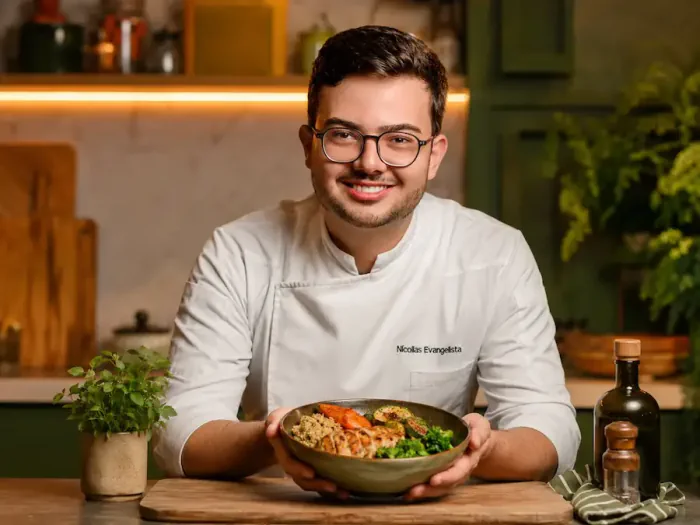 Chef Nícollas Evangelista na cozinha, segurando um dos jantares do guia